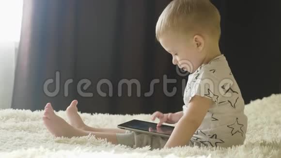 小男孩坐在床上在房间里的平板电脑上玩育和技术理念视频的预览图