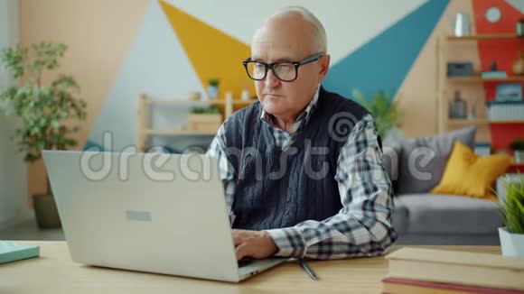 老人在家里用笔记本电脑打字然后看着相机微笑着的画像视频的预览图
