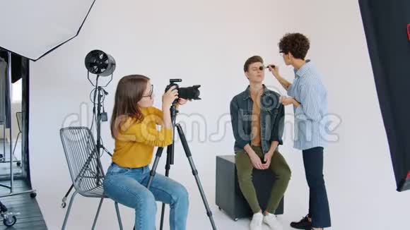 摄影师调整相机同时模特与化妆师在工作室工作视频的预览图
