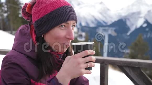 女人在山上的乡村木制露台上喝着温暖的茶女孩正在欣赏雪山的全景视频的预览图