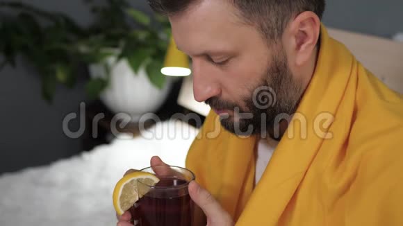 盖伊在喝红茶漂亮的年轻人病了坐在床上喝柠檬茶感冒流感疼痛视频的预览图