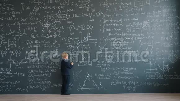 聪明的小男孩在学校的大黑板上缓慢地书写方程式视频的预览图