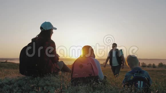 年轻的父母和两个带背包的孩子坐在山上的小径上他们喝水放松自己视频的预览图