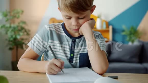 严肃的孩子在笔记本上写作业坐在书桌上视频的预览图