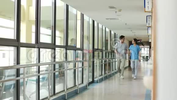 两位亚洲同事走在医院走廊上交谈视频的预览图