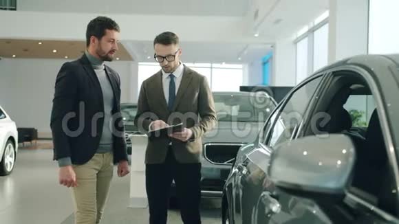 自信的销售经理与汽车经销商的男性客户交谈关注车辆反光镜视频的预览图