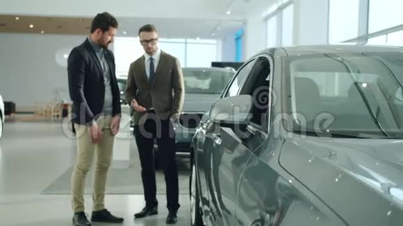 开朗的商人在展厅里买车和销售代理看汽车关注汽车镜子视频的预览图