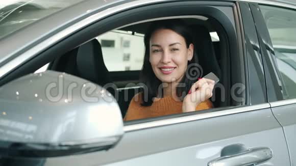 在经销商店里拿着钥匙的新车里微笑的漂亮女孩的慢镜头画像视频的预览图