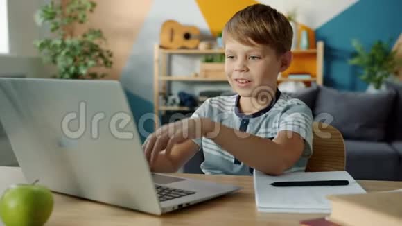 快乐的孩子用笔记本电脑打字做作业然后在笔记本上记笔记视频的预览图