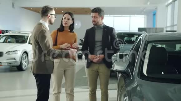 友好的专业汽车经销商与兴高采烈的客户讨论新车视频的预览图