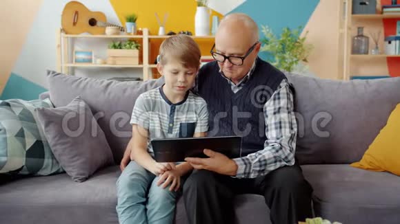 可爱的祖父和可爱的小孩在家里用平板电脑聊天视频的预览图