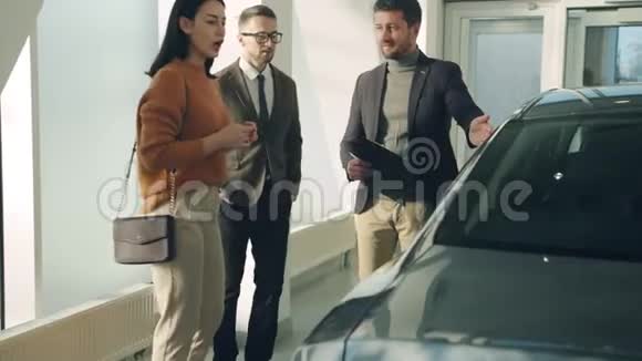 年轻的家庭夫妻在经销店选择汽车与销售经理交谈视频的预览图