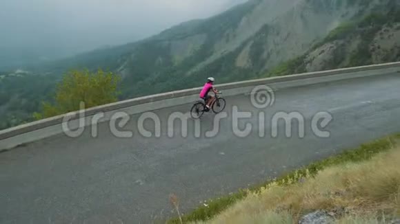 穿着粉色t恤的徒步旅行者可以在山路自行车环法路线上转弯视频的预览图