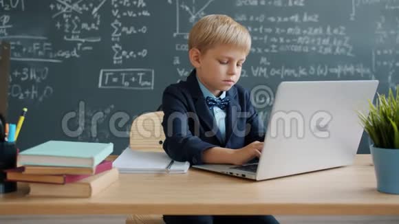 智能小孩使用笔记本电脑的慢动作然后在大学教室的书桌上写字视频的预览图