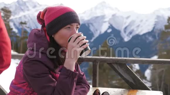 女人在山上的乡村木制露台上喝着温暖的茶女孩正在欣赏雪山的全景视频的预览图