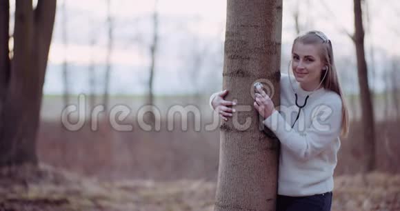 女人用听诊器检查森林里的一棵树视频的预览图