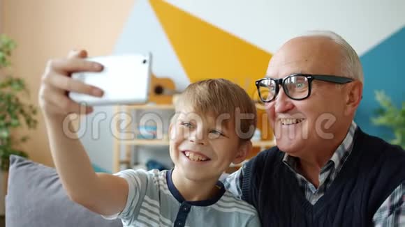 快乐的人老人和男孩在家里自拍用智能手机微笑视频的预览图