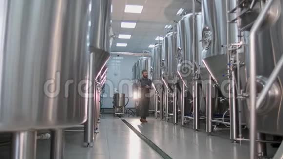 一个留着红胡子的男酿酒师走过一家工艺啤酒厂用平板电脑检查啤酒罐的证词视频的预览图