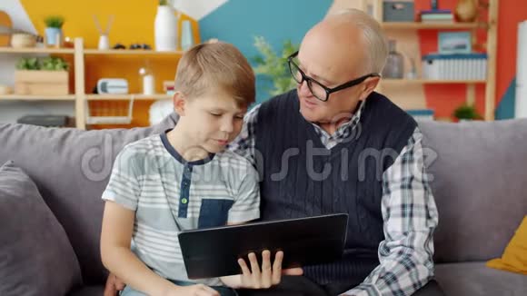 男孩使用平板电脑在家里和祖父交谈享受现代设备视频的预览图