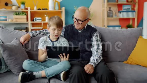 快乐的孩子和爷爷在公寓里使用平板电脑在室内交谈视频的预览图