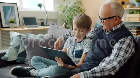 快乐的爷爷和啦啦队的孩子在家里一起玩平板电脑视频的预览图