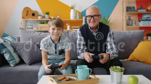 爷爷和孙子坐在家里的沙发上玩电子游戏视频的预览图