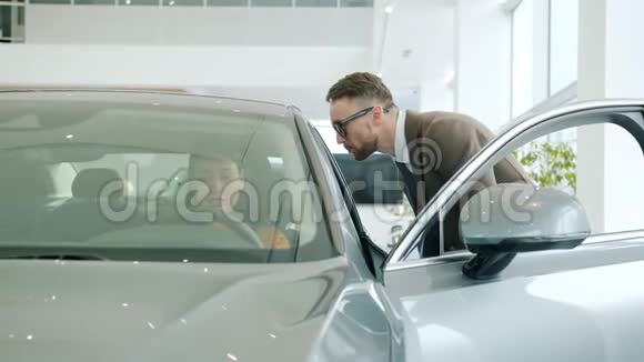 有魅力的女孩和坐在现代新车里的汽车经销商的推销员交谈视频的预览图