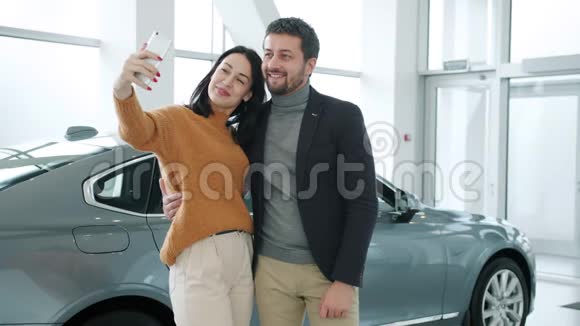 幸福夫妇在汽车经销商使用智能手机摄像头自拍的画像视频的预览图