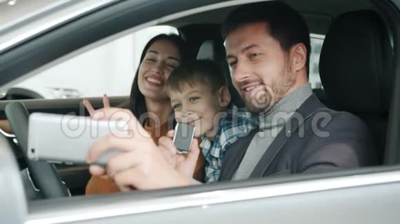快乐的年轻家庭与孩子自拍新汽车使用智能手机相机视频的预览图