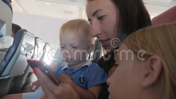 年轻的妈妈和小儿子坐在飞机上打电话旅游旅游和家庭概念视频的预览图