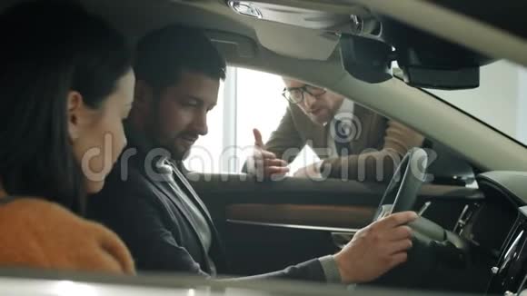 在新车里微笑的年轻夫妇和经销商的销售经理交谈视频的预览图