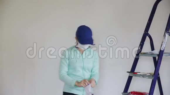 一名年轻妇女戴上呼吸器和手套开始在油漆前对墙壁进行打磨维修的背景视频的预览图