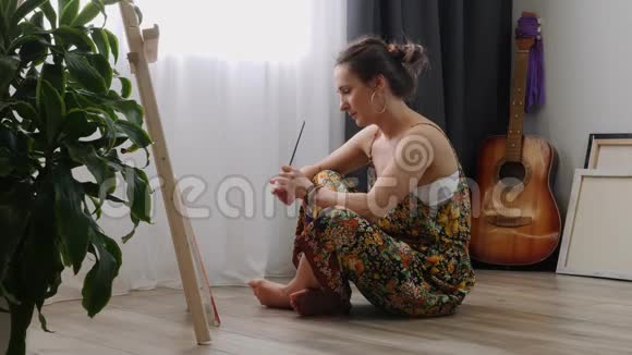 女艺术家在画布上画画用丙烯酸颜料坐在家里的地板上年轻害羞的女孩用刷子画图片内部资料视频的预览图