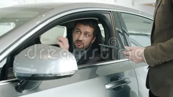 帅哥买主和坐在车里摸闪亮汽车的销售经理交谈视频的预览图