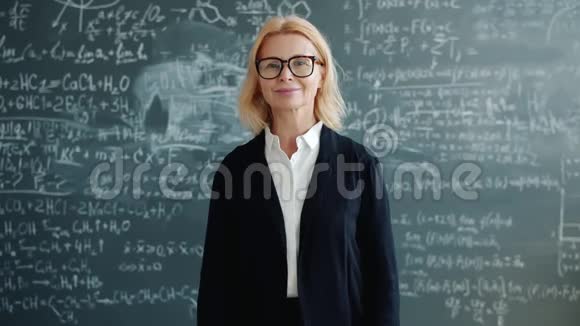 成熟的成年女性在课堂上微笑的肖像背景中有公式的黑板视频的预览图