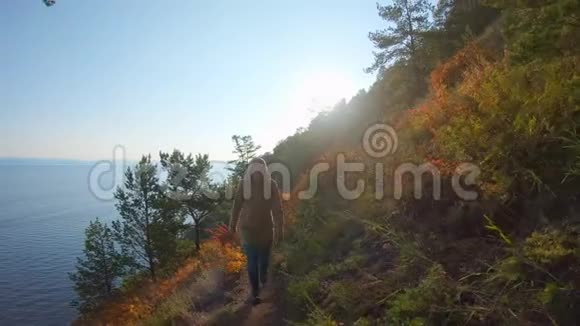 戴帽子的女孩爬上陡峭的海岸明亮的秋日照耀着视频的预览图