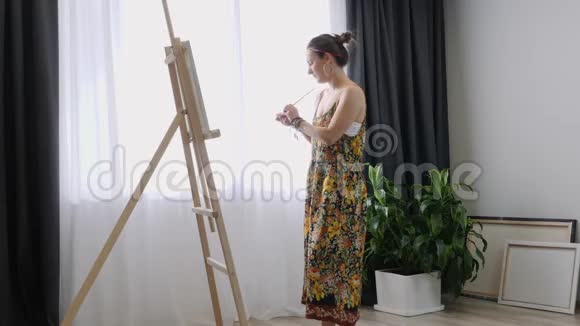 快乐迷人的女人用细刷子在画布上画画帆布站在画架上艺术家在画架上画画女性侧视p视频的预览图