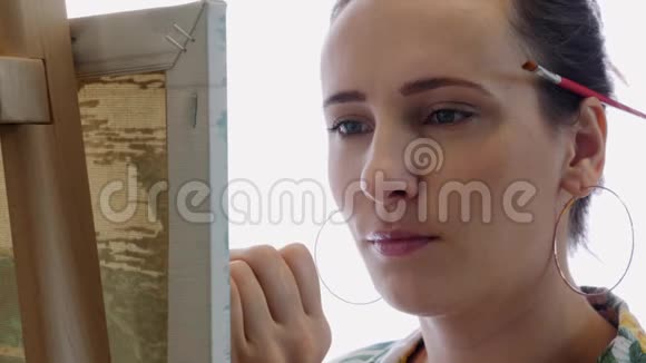 年轻迷人的女画家用细笔在画布上作画的肖像女人的脸在画架上画一幅画特写TT视频的预览图