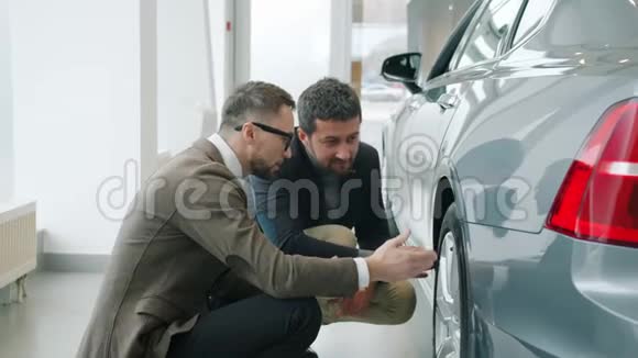 慢动作男客户和业务员在展厅讨论汽车看轮胎视频的预览图