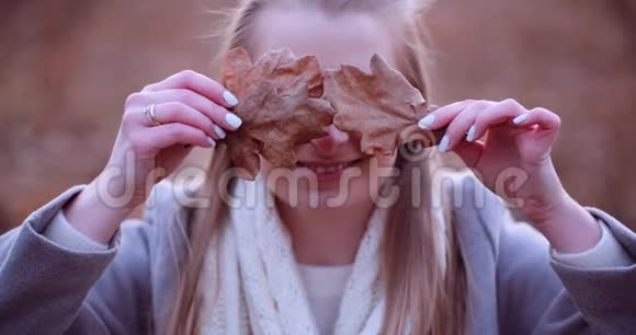 微笑的女人用秋天的树叶遮住眼睛视频的预览图