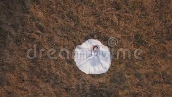 美丽可爱的新娘穿着婚纱躺在草地上空中景观视频的预览图