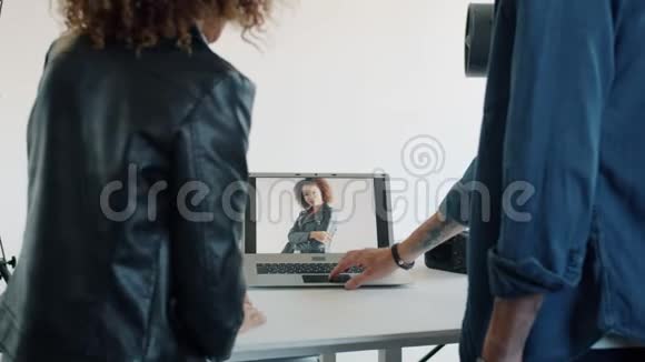 在摄影棚的笔记本电脑屏幕上观看照片的男人和女人的后视图视频的预览图