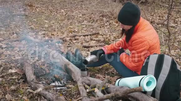 坐在森林里的树上喝着热饮料热水瓶里的茶休息的女孩视频的预览图