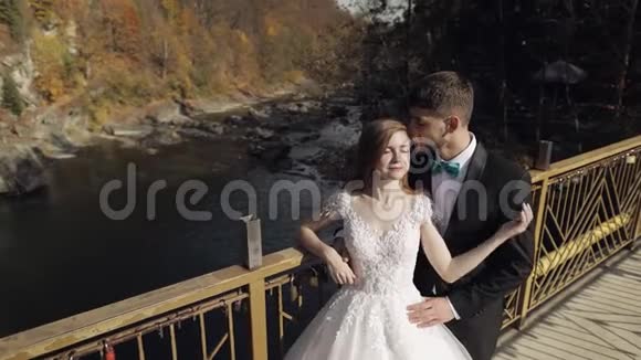 新婚夫妇一位白人新郎和新娘在一座山河上的桥上视频的预览图