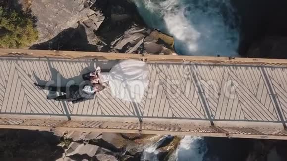 新婚夫妇新娘和新郎躺在一座山河上的桥上空中景观视频的预览图