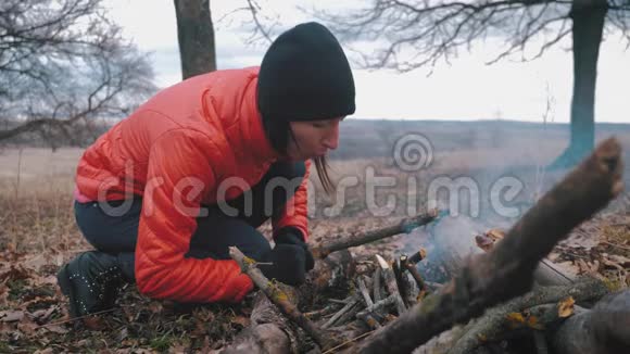 女孩游客在徒步旅行时在秋天的森林里篝火为烹饪和温暖而燃烧徒步旅行的概念视频的预览图