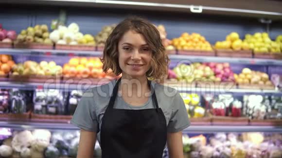 穿着黑色围裙站在超市的年轻女售货员的肖像背景是货架上的水果视频的预览图