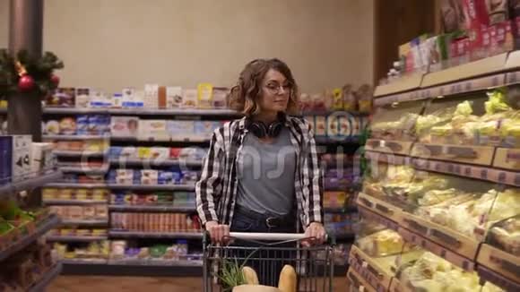 可爱的女顾客带着耳机脖子上戴着耳机在面包店买面包在店里买面包在店里看在放视频的预览图