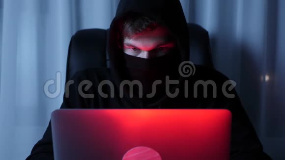 关闭男性黑客看着笔记本电脑屏幕坐在黑暗的房间戴着黑色面具的人在笔记本电脑键盘上打字职业介绍所视频的预览图