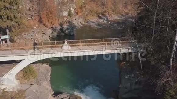 新婚夫妇新娘和新郎在一座山河上的桥上空中景观视频的预览图